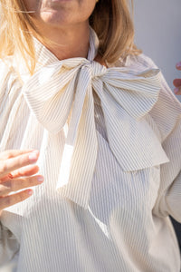 Detalle de blusa blanca con lazo grande en el cuello, tejido ligero con finas rayas, estilo elegante y femenino AnnFou