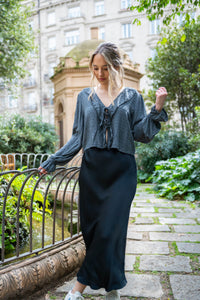 Blusa con escote pico y lacitos en gris, combinada con falda negra satinada en entorno urbano