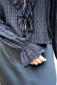 Detalle de la manga fruncida de blusa negra con textura de topos y rayas brillantes, tejido ligero y delicado