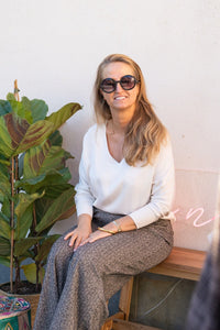 Mujer sentada con blusa de raso blanca de Ann Fou combinada con pantalón de tejido texturizado, look sofisticado y relajado