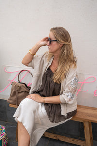 Chaqueta bomber beige con mangas de lentejuelas, look boho chic con falda satinada y bolso de ante