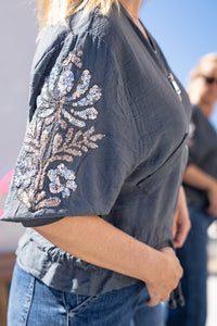 Detalle de la manga con bordado floral en lentejuelas de la bomber gris, diseño sofisticado y femenino
