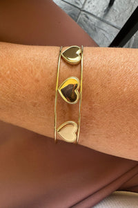 Brazalete dorado de acero inoxidable con corazones calados, lucido en la muñeca, diseño elegante y moderno