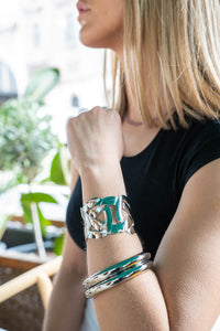 Brazalete plateado ancho con diseño entrelazado y acabado brillante, estilo moderno y llamativo sobre top negro