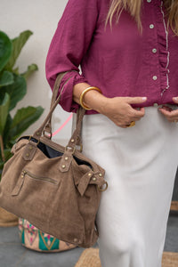 Camisa morada con cuello mao y botones, combinada con falda satinada blanca y bolso de ante marrón en primer plano
