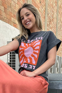Detalle de la camiseta gris Le Soleil con estampado de sol coral y rosa, diseño gráfico centrado y estilo moderno