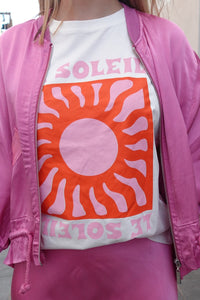 Camiseta blanca Le Soleil con estampado gráfico de sol en tonos naranja y rosa, estilo casual y llamativo