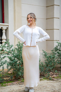 Chaqueta beige con ribete camel combinada con falda satinada, look natural y sofisticado

