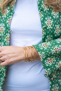 Detalle del puño de la chaqueta reversible verde con estampado vegetal, combinado con pulseras doradas y top blanco

