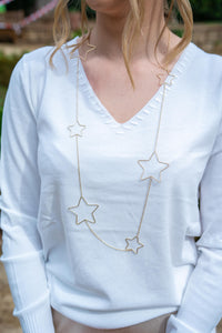 Collar largo dorado con estrellas metálicas huecas, diseño ligero y elegante sobre jersey blanco