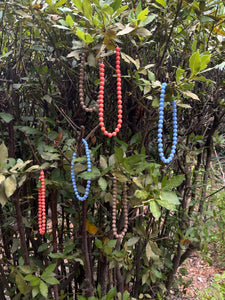 Collares de bolas en azul, coral y topo con cadena dorada de acero inoxidable, composición natural entre ramas