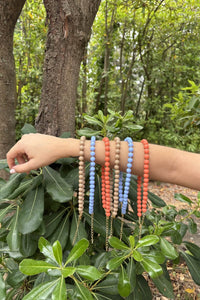 Collares de bolas en azul, coral y topo con cadena dorada, mostrados sobre el brazo en un entorno natural