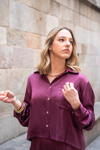 Esclava metálica dorada tipo cuff, diseño rígido y minimalista combinado con blusa satén color burdeos