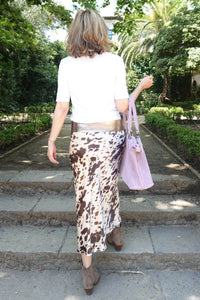 Vista trasera de la falda midi satinada con estampado de vaca, combinada con botines y bolso rosa lavanda