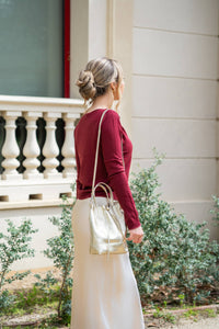 Falda satinada beige claro vista desde atrás, combinada con jersey burdeos y bolso dorado metálico
