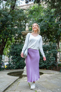 Jersey de punto blanco con escote pico y mangas largas, combinado con falda lila satinada

