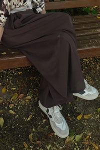 Detalle del pantalón falda marrón ancho con caída fluida, en posición sentada con zapatillas blancas