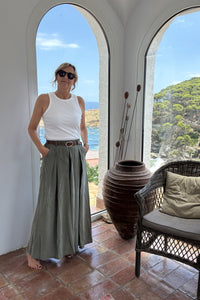 Pantalón falda verde fluido con cinturón marrón, estilo relajado en look veraniego junto a ventana mediterránea