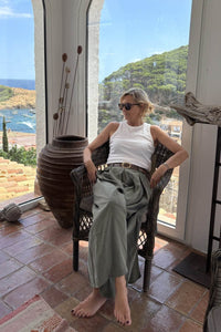 Pantalón falda verde fluido con cinturón marrón, estilo relajado en posición sentada junto a ventana mediterránea