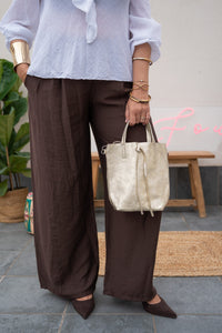 Pantalón fluido marrón con pinzas, combinado con blusa blanca de algodón y bolso metálico dorado 