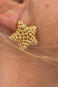 Detalle del pendiente dorado en forma de estrella con textura de bolas, fabricado en acero inoxidable