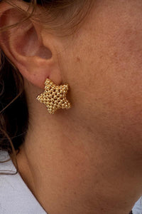 Pendiente dorado con forma de estrella en acero inoxidable, mostrado en la oreja