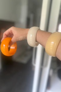 Pulseras de resina en colores naranja, beige y amarillo, colocadas en el brazo en un entorno natural