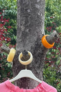 Pulseras de resina en tonos naranja, beige y amarillo, colocadas sobre las ramas de un árbol