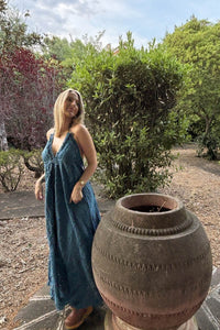 Vestido Bali azul petróleo con escote halter, corte largo fluido y bolsillos, modelo en movimiento en entorno natural